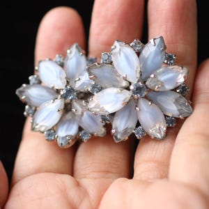 May include: A pair of silver tone earrings with a flower design. The flowers are made of white and blue iridescent stones.