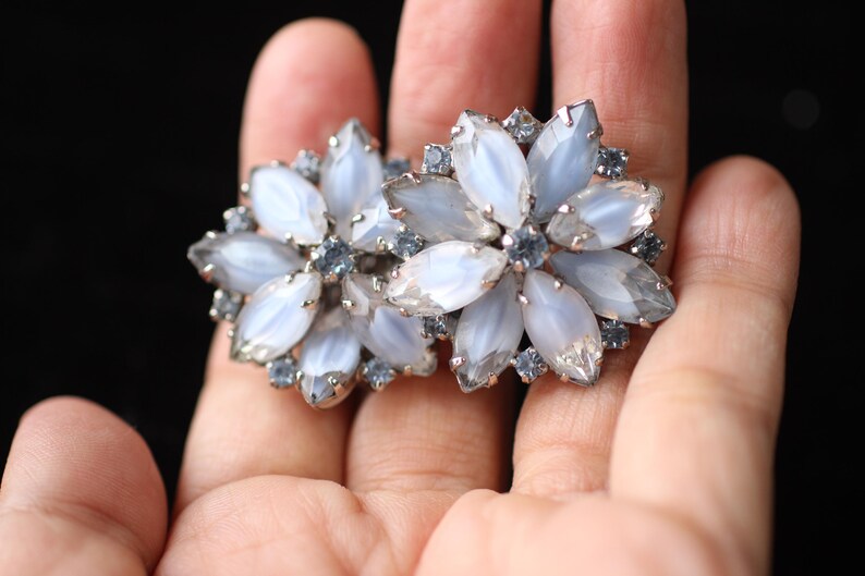 May include: A pair of silver tone earrings with a flower design. The flowers are made of white and blue iridescent stones.