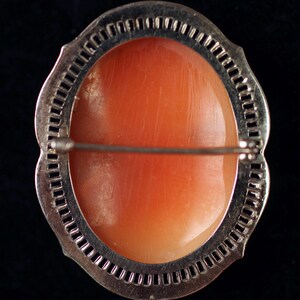May include: A silver-toned brooch with a delicate, intricate design. The brooch features a large, oval-shaped coral cameo set in the center.