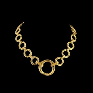 以下が含まれることがあります： 金色のネックレス。一連の相互接続された円形リンクで構成されています。 ネックレスは、大きな中央のリングと、チェーンを形成するために接続する小さなリングが特徴です。 黒い背景にジュエリーが配置されています。
