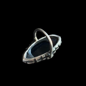 K&ouml;nnte beinhalten: Ein silberfarbener Ring mit einem ovalen, schwarzen Stein. Der Ring hat ein dekoratives, strukturiertes Band und ein einfaches, gew&ouml;lbtes Band. Der Ring ist vor einem schwarzen Hintergrund platziert.