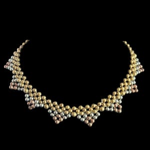 May include: A multi-tone necklace with small, round beads in gold, silver, and rose gold. The beads are arranged in a geometric pattern against a black backdrop. The necklace is designed to sit around the collarbone. The necklace is approximately 40 cm in length.