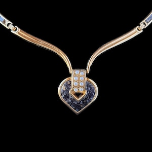 May include: Gold-toned necklace with a heart-shaped pendant. The pendant features a speckled, dark gray stone and is accented with small, round, white embellishments. The necklace has a delicate, curved design.