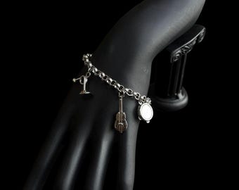 May include: Silver charm bracelet featuring a microphone, guitar, and drum charm. The bracelet is displayed on a black mannequin hand against a black background. The charms are detailed and shiny.