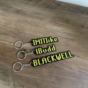 May include: Three black keychains with yellow pixelated text. The keychains read "IMMike", "Budd", and "BLACKWELL".