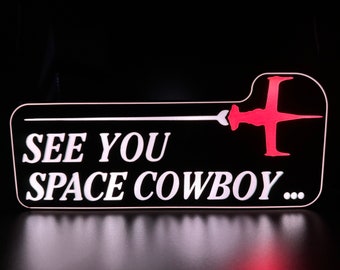 May include: A black and white sign with the text "See You Space Cowboy..." in white lettering. A red spaceship silhouette is in the top right corner.