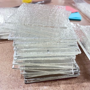 May include: A stack of clear glass squares with a textured surface. The glass squares are stacked on top of each other, creating a layered effect.