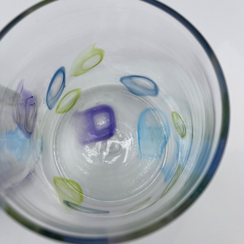 May include: Clear glass tumbler with colourful abstract designs. The tumbler features blue, green, and purple oval and square shapes. The glass has a slightly textured surface and a rounded rim.