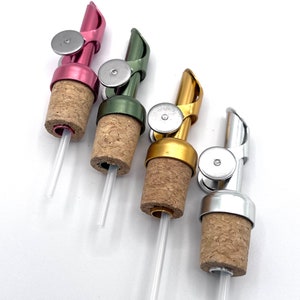 Può includere: Quattro versatori per bottiglie in metallo di diversi colori con tappi di sughero e tubi di plastica trasparente. I versatori sono argento, oro, verde e rosa.