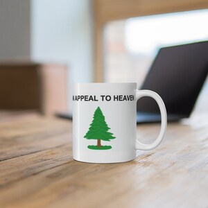Könnte beinhalten: Eine weiße Keramiktasse mit einem grünen Kiefernbaum und dem aufgedruckten Text "An Appeal to Heaven".