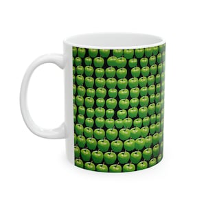 Peut inclure: Une tasse en céramique blanche avec un motif de pommes vertes. Les pommes sont disposées en un motif répétitif sur un fond noir.