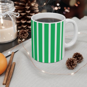 Könnte beinhalten: Eine weiße Keramiktasse mit einem grün-weiß gestreiften Design. Die Tasse ist mit Kaffee oder Tee gefüllt und es steigt Dampf aus der Oberseite auf.