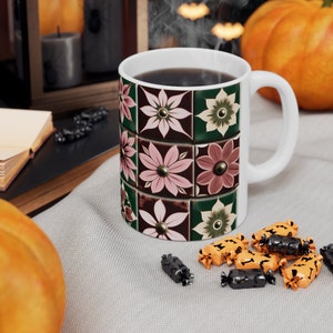 Peut inclure: Une tasse en céramique blanche avec un motif floral dans des tons de rose, vert et marron. La tasse est remplie de café et de la vapeur s'en échappe. Il y a de petits bonbons orange et noirs sur une surface grise devant la tasse.