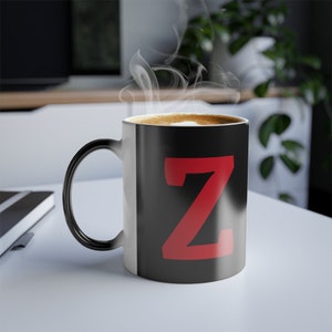 Peut inclure: Une tasse à café changeante de couleur noire et blanche avec une lettre Z rouge sur le côté noir. La tasse est remplie de café et de la vapeur s'en échappe.