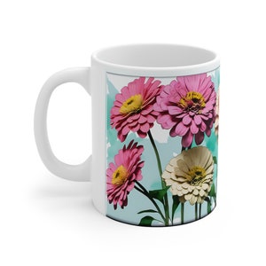 Könnte beinhalten: Weiße Keramiktasse mit einem farbenfrohen Blumendesign. Das Design zeigt rosa und weiße Blumen mit grünen Stielen und Blättern auf hellblauem Hintergrund.