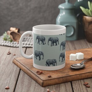 Könnte beinhalten: Weiße Keramiktasse mit einem sich wiederholenden Muster aus grauen Elefanten auf hellblauem Hintergrund.