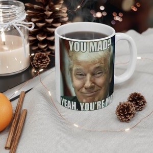 May include: White ceramic mug with a black handle. The mug features a meme image of a man with the text "You Mad? Yeah. You're Mad." printed on it.