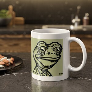Könnte beinhalten: Weiße Keramiktasse mit grünem Hintergrund und einer Schwarzweißillustration eines Frosches im Anzug und mit Krawatte. Der Text "Pep F" ist in der unteren rechten Ecke der Tasse aufgedruckt.