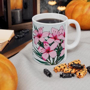 Könnte beinhalten: Eine weiße Keramiktasse mit einem Blumendesign mit rosa Blüten und grünen Blättern. Die Tasse ist mit dunklem Kaffee gefüllt.