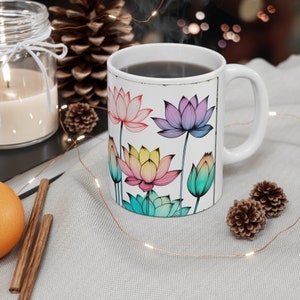 Könnte beinhalten: Eine weiße Keramik-Kaffeetasse mit einem bunten Lotusblumen-Design. Die Tasse ist mit Kaffee gefüllt und es steigt Dampf aus ihr auf.