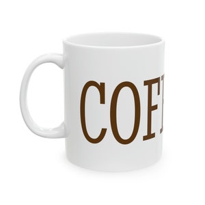 Könnte beinhalten: Weiße Keramik-Kaffeetasse mit dem Wort "COFFEE" in braunen Buchstaben.