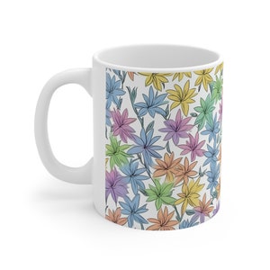 Könnte beinhalten: Weiße Keramiktasse mit einem bunten Blumenmuster. Die Blumen sind in Blautönen, Grün, Gelb, Rosa und Orange.