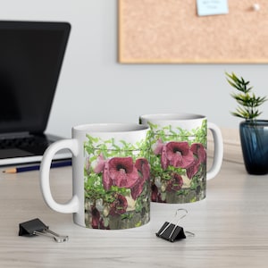 Könnte beinhalten: Zwei weiße Keramikbecher mit einem Blumendesign. Die Becher zeigen eine Nahaufnahme einer Rebe mit rosa Blüten und grünen Blättern. Die Becher stehen auf einer hellen Holzoberfläche.