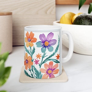 Peut inclure: Une tasse en céramique blanche avec un motif floral composé de fleurs orange, violettes, roses et vertes. La tasse a une anse blanche.