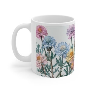 Puede incluir: Taza de cerámica blanca con un diseño floral con flores rosas, azules y amarillas con hojas verdes.