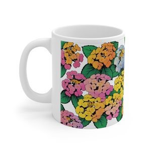 Könnte beinhalten: Weiße Keramiktasse mit einem bunten Blumenmuster. Das Muster zeigt rosa, gelbe, orange und blaue Blumen mit grünen Blättern.