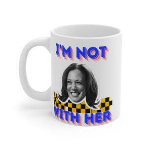 Könnte beinhalten: Weiße Keramik-Kaffeetasse mit einer blauen und rosa Grafik, die "I'm Not With Her" sagt und ein Bild von Kamala Harris zeigt. Die Grafik hat ein kariertes Muster darunter.