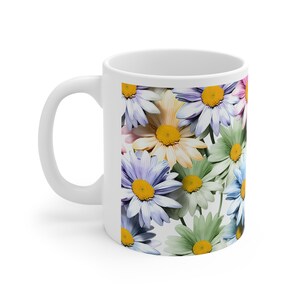 Peut inclure: Une tasse en céramique blanche avec un motif floral coloré composé de marguerites dans des tons de bleu, vert, jaune et rose.