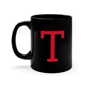 Peut inclure: Une tasse en céramique noire avec une lettre majuscule "T" rouge imprimée sur le devant.