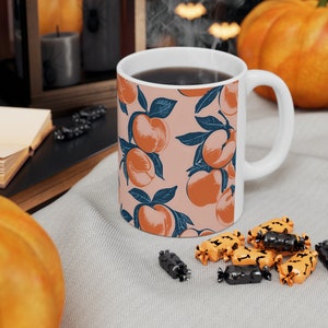 Könnte beinhalten: Eine weiße Keramiktasse mit einem Pfirsichmuster. Die Tasse ist mit Kaffee gefüllt und es steigt Dampf aus ihr auf. Die Tasse steht auf einer grauen Oberfläche mit ein paar Süßigkeiten, die um sie herum verstreut sind.