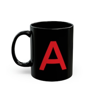 Peut inclure: Une tasse en céramique noire avec une grande lettre "A" rouge imprimée sur le devant.