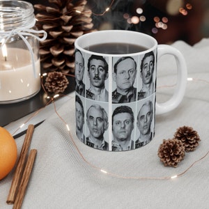 Könnte beinhalten: Weiße Keramiktasse mit schwarzem Henkel. Die Tasse zeigt eine Collage aus Schwarzweiß-Fahndungsfotos von Männern mit Nummern unter jedem Foto.