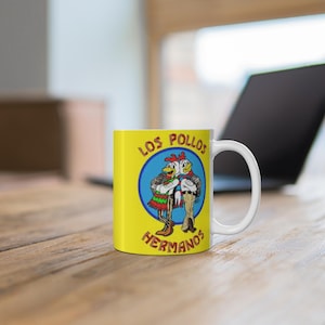 Peut inclure: Une tasse en céramique blanche avec un fond jaune et un cercle bleu représentant deux poulets de dessin animé avec le texte "Los Pollos Hermanos" en rouge et noir.