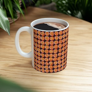 Könnte beinhalten: Weiße Keramiktasse mit schwarzem Hintergrund und einem sich wiederholenden Muster aus orangen Zitrusfrüchtescheiben. Die Tasse ist mit Kaffee gefüllt.