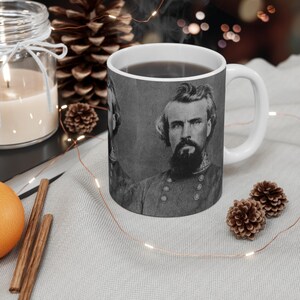 May include: A white ceramic mug with a black and white photo of a man with a beard and mustache. The man is wearing a military uniform. The mug is filled with coffee.