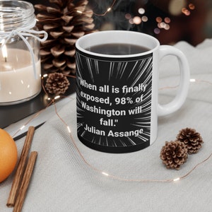Könnte beinhalten: Eine schwarz-weiße Kaffeetasse mit einem Zitat von Julian Assange, das lautet: "Wenn alles endlich aufgedeckt ist, werden 98 % von Washington fallen."