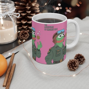 May include: A pink ceramic mug with a white handle features a cartoon illustration of a green frog wearing a military uniform and a pilot's helmet. The text "The Adventures of Sergeant Pepe" is printed on the mug.