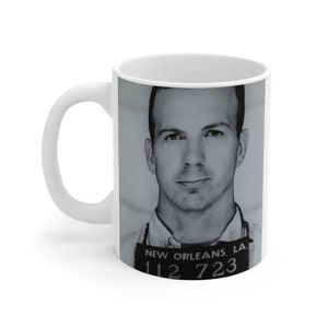 May include: White ceramic mug featuring a black and white image of a man. The image includes a mugshot with the text "NEW ORLEANS, LA." and the numbers "112 723". The mug has a white handle.
