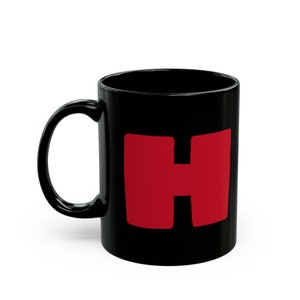 Peut inclure: Une tasse en céramique noire avec une lettre H rouge sur le devant.