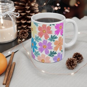 Könnte beinhalten: Weiße Keramiktasse mit einem bunten Blumenmuster. Die Tasse ist mit Kaffee gefüllt und Dampf steigt aus der Oberseite auf.