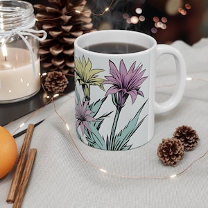 Peut inclure: Une tasse en céramique blanche avec un motif floral composé de fleurs roses, jaunes et vertes. La tasse est remplie de café noir et a une poignée blanche.