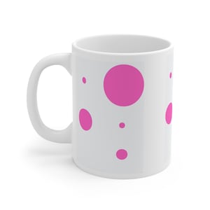 Puede incluir: Taza de cerámica blanca con un patrón de lunares rosas. La taza tiene un círculo rosa grande en el centro y círculos rosas más pequeños alrededor.