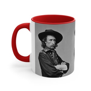 May include: A black and white photo of a man in a military uniform and hat. He is standing with his arms crossed and looking to the side. The photo is printed on a white ceramic mug with a red rim.
