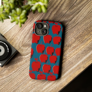 May include: A blue phone case with a pattern of red apples. The case has a camera lens cutout and a white border.