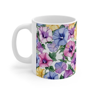 Könnte beinhalten: Weiße Keramiktasse mit einem Blumenmuster. Das Muster zeigt lila, rosa, blaue und gelbe Blumen auf weißem Hintergrund.