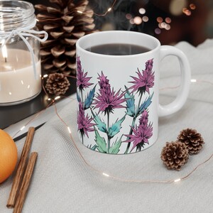 Könnte beinhalten: Eine weiße Keramiktasse mit einem Blumendesign mit rosa und blauen Blumen. Die Tasse ist mit Kaffee gefüllt und Dampf steigt aus der Oberseite auf.